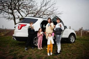 mãe com filhos bebe chá ao ar livre perto de carro suv branco. foto