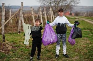 irmãos com saco de lixo coletando lixo durante a limpeza nas vinhas. conservação ambiental e ecologia, reciclagem. foto