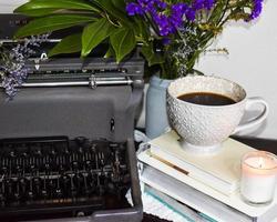 máquina de escrever vintage com flores roxas, uma pilha de livros, uma vela e uma caneca de café foto