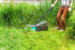 homem cortando grama verde com cortador de grama no quintal. fundo de estilo de vida do país de jardinagem. bela vista no gramado de grama verde fresca à luz do sol, paisagem de jardim na primavera ou verão. foto