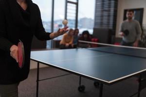 dois jovens iniciantes jogando tênis de mesa no moderno espaço de escritório criativo grupo de pessoas tem reunião e brainstorming em segundo plano foto