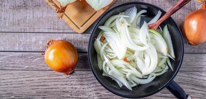 fatias de cebola branca na panela para cozinhar e cebola branca fresca no fundo cinza. foto