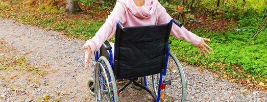 mulher jovem deficiente feliz em cadeira de rodas na estrada no parque hospitalar desfrutando de liberdade. menina paralisada na cadeira inválida para pessoas com deficiência ao ar livre na natureza. conceito de reabilitação. foto