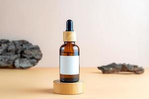 frasco conta-gotas cosmético de vidro âmbar com rótulo em branco no pódio de madeira redondo. design de produtos de beleza natural, branding. cosméticos de maquete foto