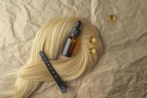 um óleo essencial de tratamento capilar para alisar o cabelo e um modelador de ondulação de cabelo deitado sobre um fundo de papel artesanal marrom foto
