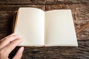 foto recortada da mão de alguém tocando um livro de couro diário aberto com espaço em branco na mesa de madeira. o conceito de educação e aprendizagem.