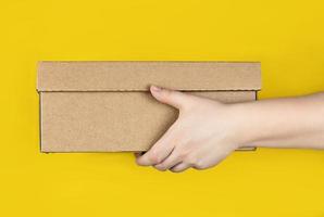 grande caixa de papelão nas mãos em um fundo amarelo na moda. foto horizontal. conceito - entrega de pedidos em sua casa por correio, recebimento de encomendas, distância segura