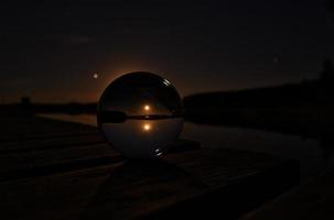 bola de vidro em um cais de madeira em um lago sueco à noite. estrelas e lua foto