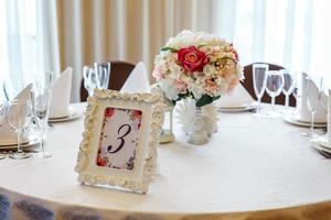 mesa chique para jantar com composição de flores no restaurante, fundo interior de luxo. decoração de banquete elegante de casamento e itens para alimentos organizados pelo serviço de catering na mesa branca. foto