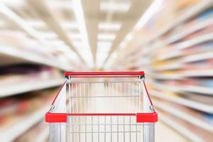 corredor de supermercado fundo desfocado com carrinho de compras vermelho vazio foto