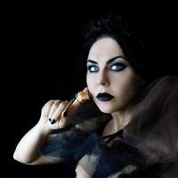 mulher gótica de cabelo escuro com maquiagem de lábios pretos e rosa seca na mão
