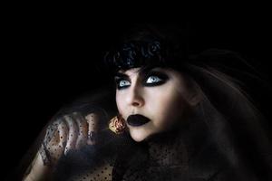 mulher gótica de cabelo escuro com maquiagem de lábios pretos e rosa seca na mão