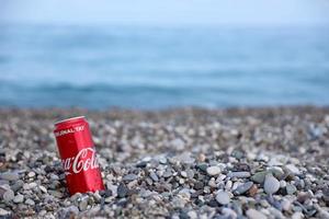 antalya, turquia - 18 de maio de 2021 lata vermelha original da coca cola encontra-se em pequenas pedras redondas perto da costa do mar. coca-cola na praia turca foto