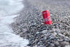 antalya, turquia - 18 de maio de 2021 lata vermelha original da coca cola encontra-se em pequenas pedras redondas perto da costa do mar. coca-cola na praia turca foto