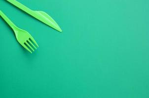 talheres de plástico descartáveis verdes. garfo e faca de plástico estão sobre uma superfície de fundo verde foto