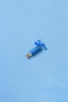 cartão de memória flash usb azul brilhante com um laço azul repousa sobre um cobertor de tecido de lã azul claro macio e peludo. design de presente feminino clássico para um cartão de memória foto