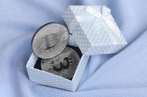 o bitcoin prateado está em uma pequena caixa de presente azul com um pequeno laço em um cobertor feito de tecido de lã azul claro macio e fofo com um grande número de dobras em relevo foto