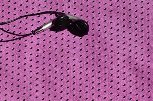 os fones de ouvido pretos repousam sobre a roupa esportiva roxa de fibra de nylon de poliéster. o conceito de ouvir música durante o treinamento esportivo com tecnologia moderna foto