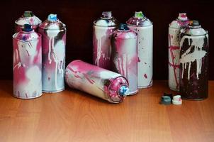 natureza morta com um grande número de latas de spray coloridas usadas de tinta aerossol na superfície de madeira tratada na oficina de grafite do artista. latas sujas e manchadas para arte em spray foto