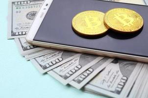 bitcoins está em um smartphone e notas de cem dólares em um fundo azul claro foto