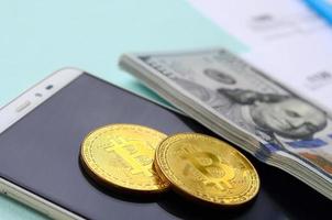 bitcoins encontra-se com os formulários de imposto, notas de cem dólares e smartphone em um fundo azul claro. restituição do Imposto de Renda foto