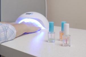 três garrafas de esmalte transparente incolor no fundo das mãos femininas em gel uv led unha lâmpada branca para secagem de manicure foto