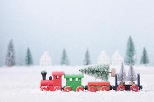 árvore de natal no trem de brinquedo estava correndo pela neve no campo de fundo de paisagem natural foto