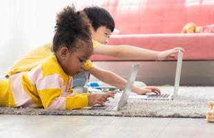 crianças felizes com laptop deitado no tapete na sala de estar em casa foto