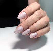 manicure branca feminina nas unhas contra um fundo escuro foto