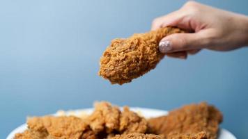 mão segurando coxinhas, frango frito crocante em chapa branca sobre fundo azul. foto