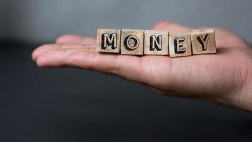 uma mão segurando a caixa de madeira com texto de dinheiro no fundo preto, banco de dinheiro e conceito de finanças, atirar com espaço de cópia para texto e design foto