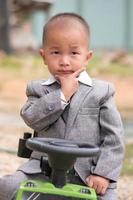 crianças felizes sentadas em seu carro de brinquedo com fundo de desfoque de terno, lindo menino asiático foto
