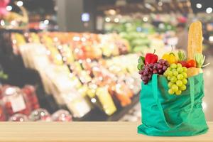 frutas e legumes frescos em sacola de compras verde reutilizável no tampo da mesa de madeira com supermercado desfocado fundo desfocado com luz bokeh foto