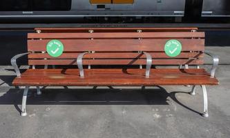 os adesivos de ponto verde estão sendo colocados na cadeira de parque de madeira para mostrar às pessoas onde elas podem se sentar enquanto mantêm o distanciamento social. foto