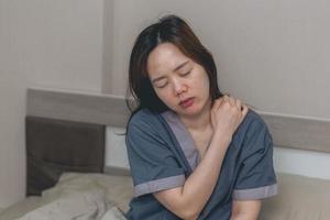 mulher asiática está segurando as mãos na cabeça com dor na cama em casa, mulheres jovens têm fortes dores de cabeça de enxaquecas, conceito de saúde e doença foto
