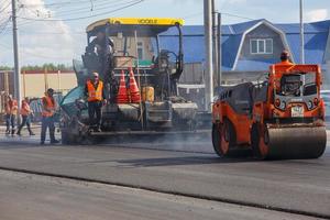 tula, rússia 16 de maio de 2021 processo de asfaltamento, máquina de pavimentação de asfalto e rolo compactador durante obras de construção de estradas, no dia de verão foto