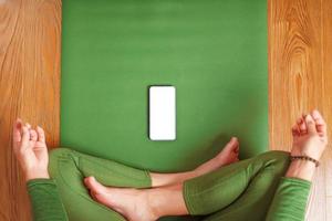 uma mulher assiste a aulas de ioga em seu smartphone enquanto está sentada em um colchonete verde foto