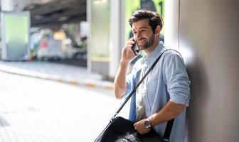 o homem de negócios falando no telefone inteligente a caminho. sentindo-se feliz e relaxante, casual jovem empresário vestindo paletó e bolsa de ombro. foto