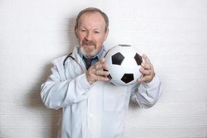 bonito médico idoso segurando uma bola de futebol, promovendo esportes foto