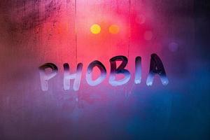 a palavra fobia escrita à mão na superfície de vidro de janela nevoenta molhada com luzes de fundo vermelho-azul foto