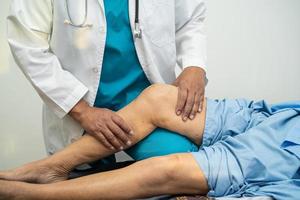 Médico fisioterapeuta examinando, massageando e tratando o joelho e a perna do paciente sênior no hospital de enfermagem da clínica médica ortopedista. foto