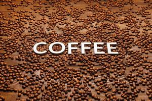palavra café colocado com letras prateadas na superfície de madeira coberta com grãos de café foto