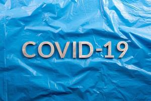 a palavra covid-19 colocada com letras de alumínio em fundo de filme plástico azul amassado em composição plana leiga, diretamente acima da vista foto