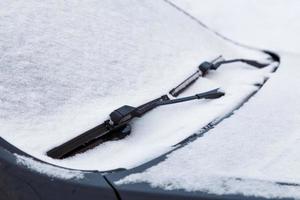 pára-brisa do carro e lâminas de água do limpador congeladas e cobertas de neve na luz do dia nublado de inverno foto
