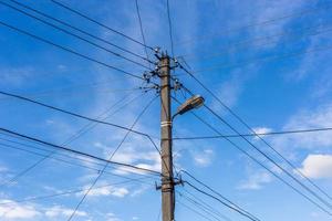poste de luz de concreto com muitos cabos conectados radialmente no céu azul com nuvens de penas ao fundo, composição centrada. foto