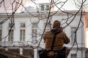 fotógrafo profissional sorrateiro fotografando a fachada de um edifício branco privado da cerca sob pequenos brcnches. foto