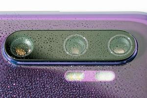 lente roxa da câmera do telefone coberta com pequenas gotas de água - close-up com foco seletivo e desfoque foto