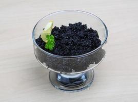 caviar preto em uma tigela sobre fundo de madeira foto