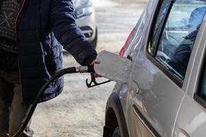 mão de velho no casaco azul quente reabastecendo carro metálico cinza no posto de gasolina durante o dia - close-up com foco seletivo foto