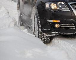 veículo preto movendo-se pela neve profunda derrapando, a roda do carro girando e vomitando pedaços de neve ele tenta ganhar tração na estrada escorregadia. foto